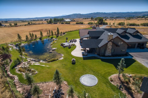 Aerial view of a spacious modern home with a pond, landscaped yard, and surrounding fields.